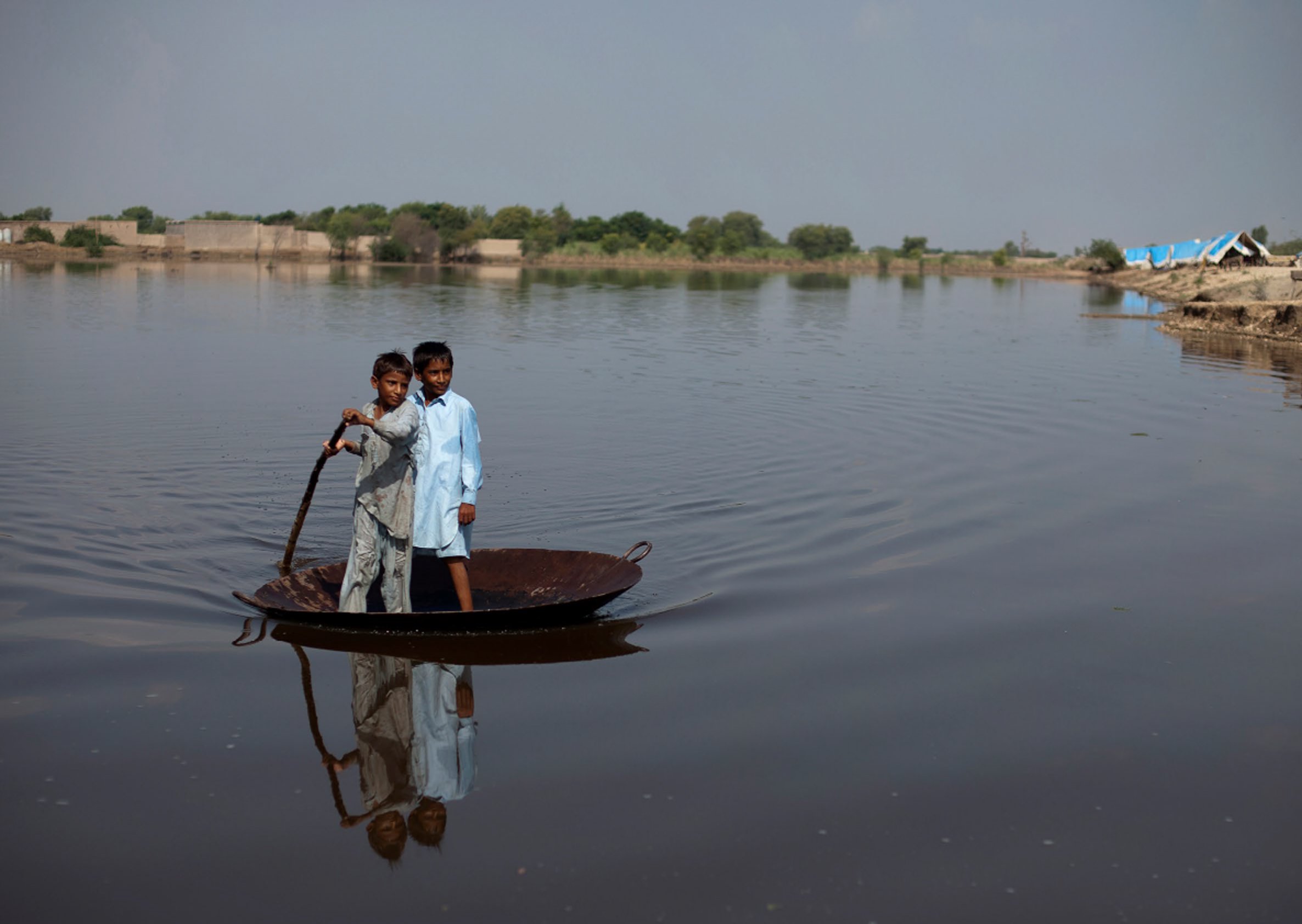Boys use a large steel pot as a raft to cross an expanse of flood water in Pakistan in 2011