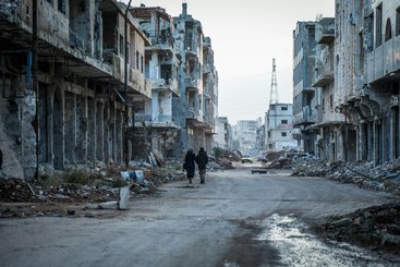 Two people walk down a destroyed street in Daraa, Syria